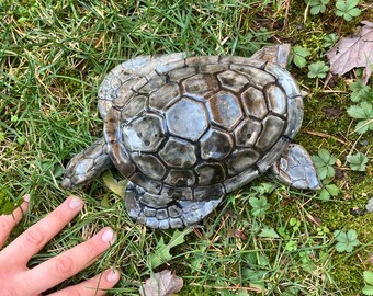 May include: A ceramic turtle sculpture with a dark green glaze and a detailed shell. The turtle is sitting on a bed of green grass.