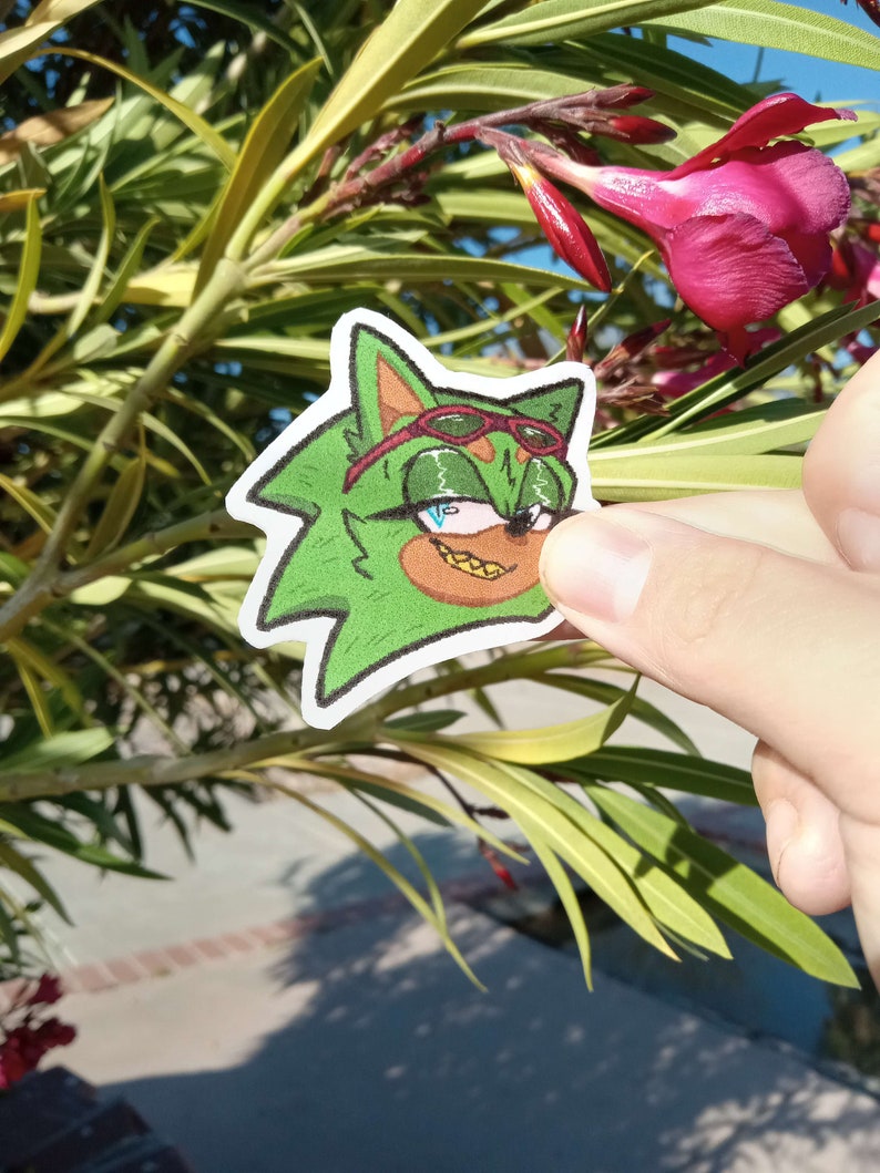 K&ouml;nnte beinhalten: Ein gr&uuml;ner Comic-Charakter mit einem roten Bandana, Sonnenbrille und einem goldenen Zahn. Der Charakter h&auml;lt einen rot-wei&szlig; gestreiften Lollipop.