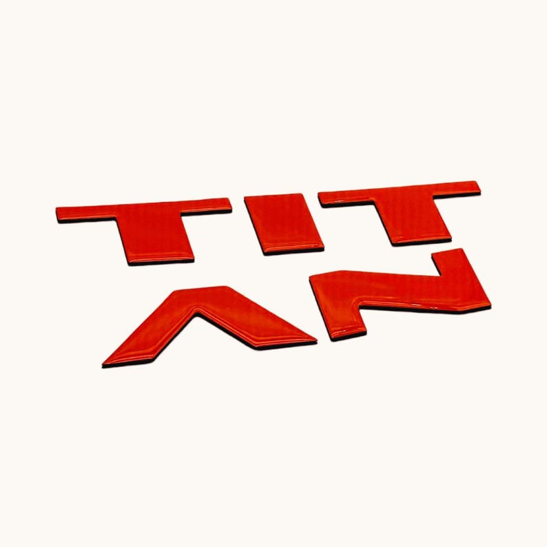 May include: Red plastic letters spelling out the word "TITAN" in a bold, three-dimensional style. The letters are arranged in a staggered formation, creating a dynamic and eye-catching design.