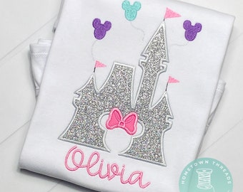 Puede incluir: Camiseta blanca con un diseño de castillo plateado brillante, un lazo rosa y el nombre "Olivia" en escritura rosa. El diseño incluye globos morados y turquesas con forma de Mickey Mouse y banderas rosas. La camiseta está doblada.