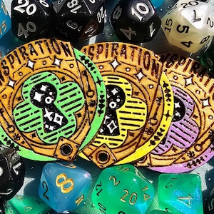 May include: Three wooden tokens with the word "Inspiration" written around the edge. Each token has a different colored background: green, yellow, and purple. The tokens are surrounded by a variety of dice in different colors and shapes.
