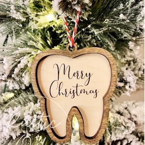 May include: A wooden Christmas ornament shaped like a tooth with the text "Merry Christmas" engraved on it. The ornament is hanging from a red and white twine.