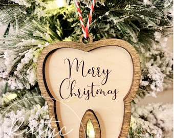 May include: A wooden Christmas ornament shaped like a tooth with the text "Merry Christmas" engraved on it. The ornament is hanging from a red and white twine.