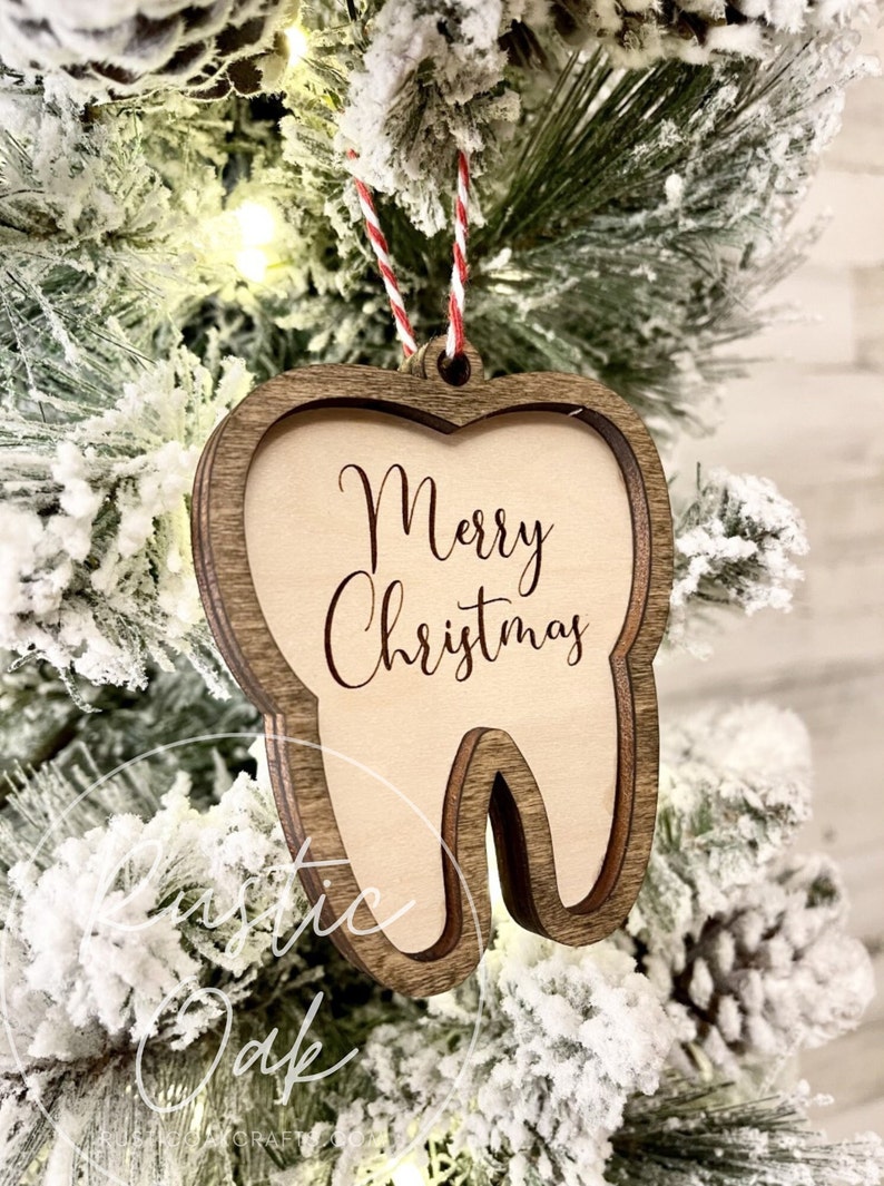 May include: A wooden tooth-shaped Christmas ornament with the words "Merry Christmas" inscribed on it. The ornament is hanging on a Christmas tree.