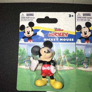 Peut inclure: Une figurine en plastique de Mickey Mouse dans un emballage en plastique transparent. La figurine porte un short rouge avec deux cercles blancs, des chaussures noires et des gants blancs. L'arri&egrave;re-plan est un parc vert avec un toboggan et une balan&ccedil;oire. L'emballage porte une &eacute;tiquette d'avertissement indiquant "RISQUE D'&Eacute;TOUFFEMENT - Petites pi&egrave;ces. Ne convient pas aux enfants de moins de 3 ans."
