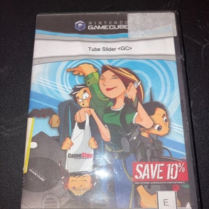 Peut inclure: Une boîte de jeu vidéo GameCube avec une illustration de quatre personnes en dessin animé bleu, blanc et vert. Le jeu s'appelle "Tube Slider <GC>" et est une exclusivité GameStop. La boîte a un autocollant "Save 10%" dessus.
