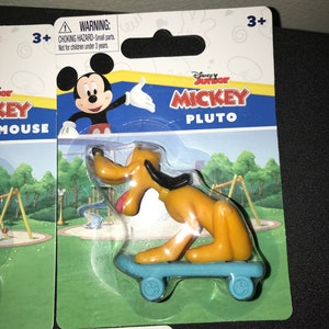 Peut inclure: Une figurine en plastique de Pluto de Mickey Mouse de Disney Junior. Pluto est sur une planche &agrave; roulettes bleue avec des roues Mickey Mouse. L'emballage est bleu, jaune et rouge avec les mots "Disney Junior Mickey Pluto" dessus. Une &eacute;tiquette d'avertissement indique "Risque d'&eacute;touffement - Petites pi&egrave;ces. Ne convient pas aux enfants de moins de 3 ans."
