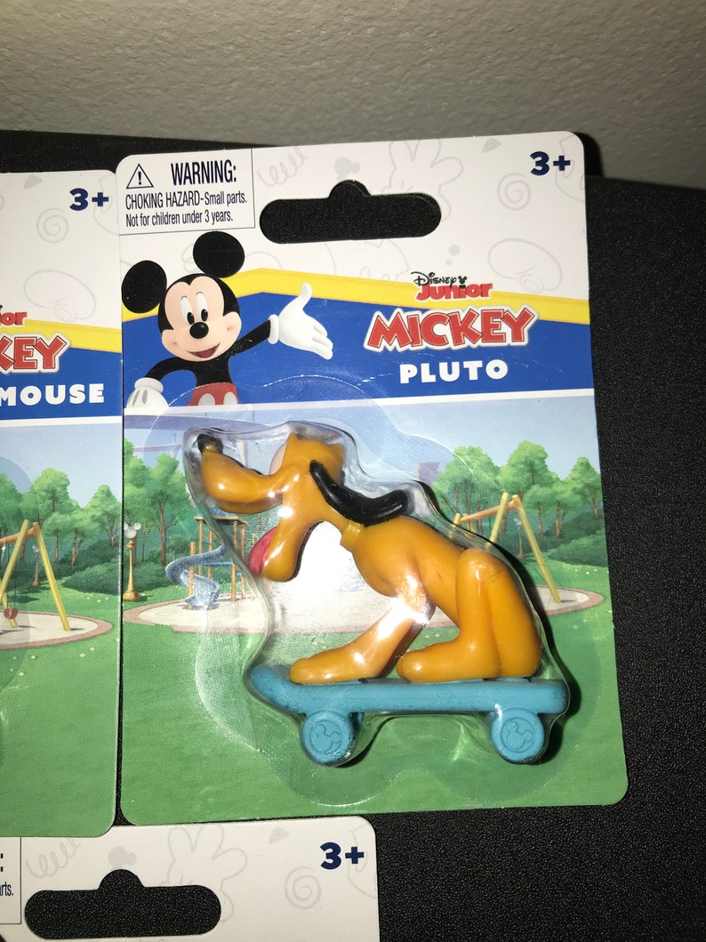 Peut inclure: Une figurine en plastique de Pluto de Mickey Mouse de Disney Junior. Pluto est sur une planche &agrave; roulettes bleue avec des roues Mickey Mouse. L'emballage est bleu, jaune et rouge avec les mots "Disney Junior Mickey Pluto" dessus. Une &eacute;tiquette d'avertissement indique "Risque d'&eacute;touffement - Petites pi&egrave;ces. Ne convient pas aux enfants de moins de 3 ans."