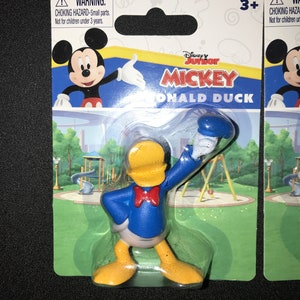 Peut inclure: Une figurine en plastique de Donald Duck de Mickey Mouse Clubhouse de Disney Junior. Donald Duck porte sa chemise de marin bleue signature avec un n&oelig;ud papillon rouge et un pantalon jaune. La figurine est emball&eacute;e dans une bo&icirc;te &agrave; bulles en plastique avec un fond vert et blanc. L'emballage comprend un avertissement de risque d'&eacute;touffement et une recommandation d'&acirc;ge de 3 ans et plus.
