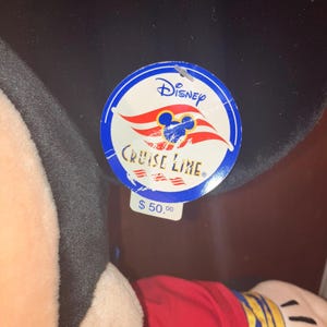 May include: A Mickey Mouse soft toy in a red shirt with yellow and blue details. The toy has a black head and ears, and a Disney Cruise Line tag attached.