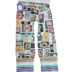 May include: A pair of teal blue leggings with a colorful camera print. The leggings have a striped waistband and cuffs in shades of blue, green, and gray.