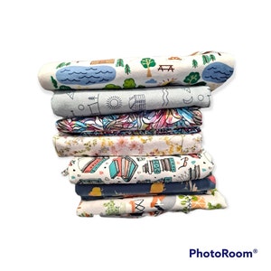 May include: A stack of eight fabric panels with various colorful patterns. The patterns include a blue and white wave design, a floral design, a design with books, and a design with a campfire and trees.