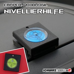 Op de afbeelding: Een zwarte nivelleerhulp voor campers en caravans. Het apparaat heeft een heldere, cirkelvormige waterpas met een blauwe achtergrond en witte markeringen. De tekst "CAMPER, WOHNMOBIL NIVELLIERHILFE" staat bovenaan. De website "SCHWARZTEE82.de" staat onderaan.