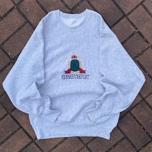 May include: A gray sweatshirt with a crest embroidered on the front. The crest features a crown, a letter K, and the text "KENNEBUNKPORT".
