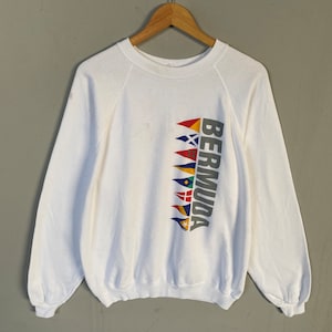 May include: White sweatshirt with a graphic of the word "BERMUDA" printed vertically with a row of colorful flags.