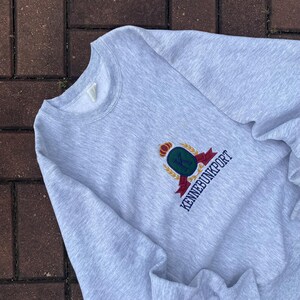 May include: Gray sweatshirt with a crest embroidered on the front. The crest features a crown, a letter K, and the text "KENNEBUNKPORT".