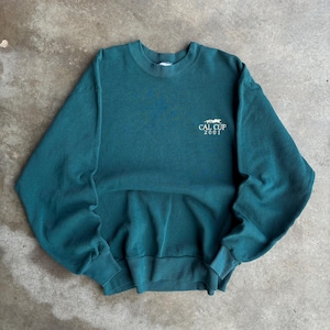 May include: Teal crewneck sweatshirt with the text "CAL CUP 2001" in white. The sweatshirt has a classic fit with ribbed cuffs and hem. The fabric appears to be a soft, medium-weight material.