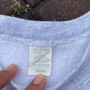 May include: A gray sweatshirt with a white tag that reads "007317.601654 09198100 1191 CA076 95% COTTON 5% POLYESTER MADE IN USA AN14666 CARE OVER MEDIUM".