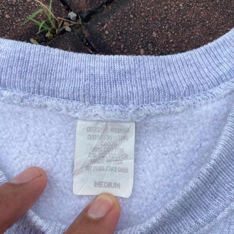 May include: A gray sweatshirt with a white tag that reads "007317.601654 09198100 1191 CA076 95% COTTON 5% POLYESTER MADE IN USA AN14666 CARE OVER MEDIUM".
