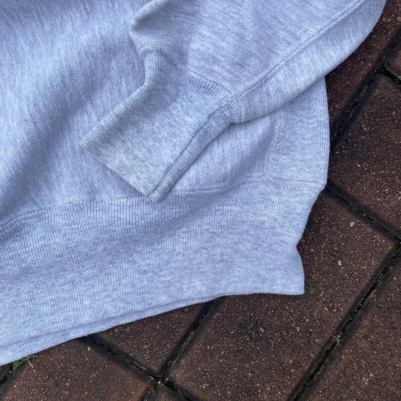 May include: A close-up of the gray knit fabric of a sweater. The fabric is soft and textured, with a ribbed knit pattern. The sweater has a long sleeve and a ribbed cuff.