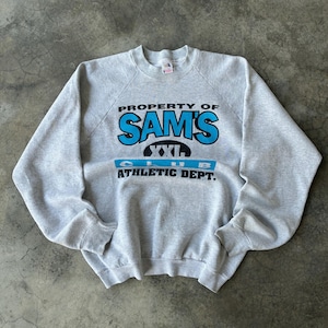 May include: A light gray sweatshirt with the text "PROPERTY OF SAM'S CLUB ATHLETIC DEPT." in blue and black. The sweatshirt is a crew neck style and appears to be vintage.