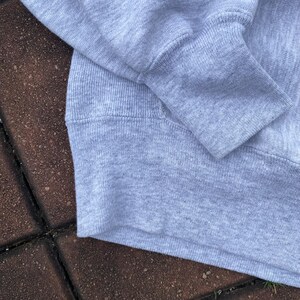 May include: Close-up of the gray fabric of a sweatshirt. The fabric is soft and textured, with a ribbed knit pattern.