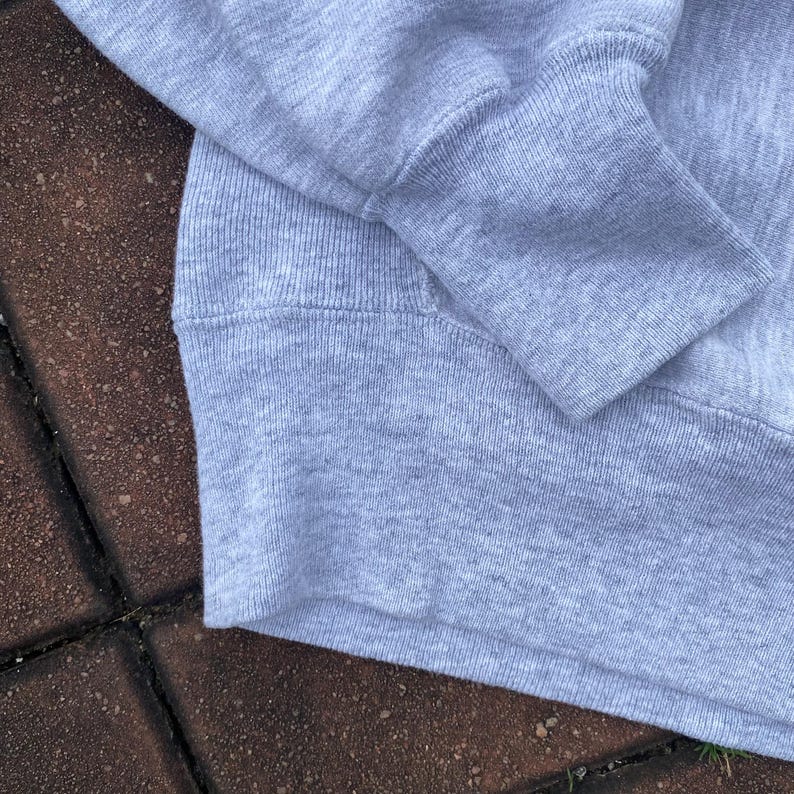 May include: Close-up of the gray fabric of a sweatshirt. The fabric is soft and textured, with a ribbed knit pattern.