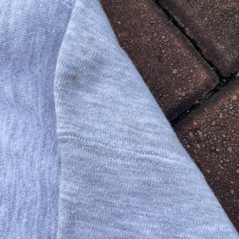 May include: Close-up of a light gray sweatshirt fabric. The fabric has a subtle texture and a slightly faded appearance.