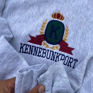 May include: Gray sweatshirt with a navy blue embroidered logo featuring a crown, the letter K, and the text "Kennebunkport".
