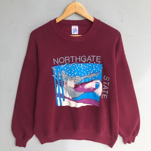 以下が含まれることがあります： ワインレッドのトレーナーに、雪景色と「Northgate State」の文字がプリントされています。