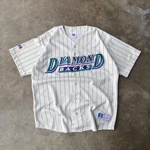 May include: A white baseball jersey with thin purple pinstripes, featuring the text DIAMONDBACKS in teal and purple lettering across the chest. The shirt has a button-down front, short sleeves, a Russell Athletic logo on the sleeve, and a patch at the hem.