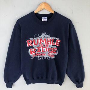 May include: A navy blue sweatshirt with a red graphic print that says "Rumble on the Ridge" with the text "Adena, Ohio" and "2002" below. The graphic also includes a silhouette of a person riding an ATV.