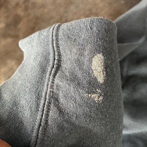 May include: A dark gray fabric sleeve featuring a prominent ribbed cuff and a visible light-colored, textured stain or discoloration on the outer surface of the material. The fabric appears to be a soft, knit textile with a visible weave pattern.