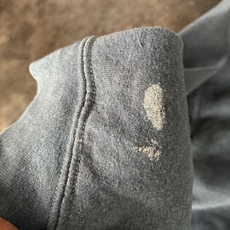 May include: A dark gray fabric sleeve featuring a prominent ribbed cuff and a visible light-colored, textured stain or discoloration on the outer surface of the material. The fabric appears to be a soft, knit textile with a visible weave pattern.