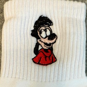 May include: White ribbed sock featuring an embroidered cartoon character in black, red, and white. The character has a black head, a red outfit, and a white face. The sock is made of a soft, ribbed material.