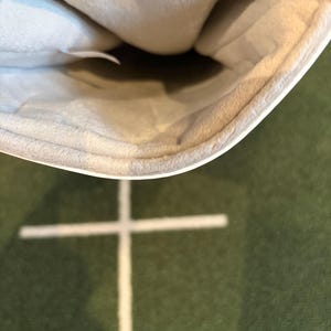 May include: A white, curved, open-ended sleeve or pouch featuring a soft, light beige, plush interior lining. The exterior is smooth and white, while the inner material has a textured, fuzzy appearance, creating a contrast in surface finish.
