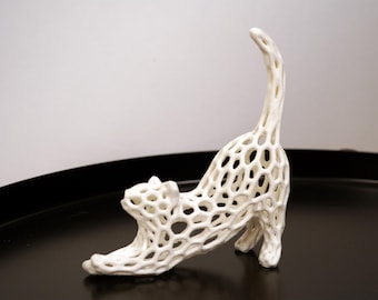 Op de afbeelding: Witte keramische kattenbeeld met een traliewerk ontwerp. De kat is in een uitgestrekte houding met zijn staart omhoog.