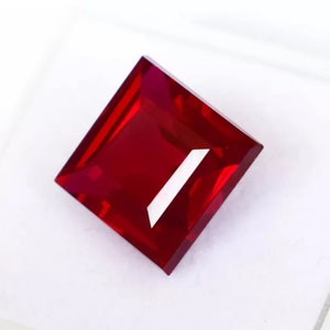 Puede incluir: Una piedra preciosa cuadrada de color rojo intenso con un acabado pulido.