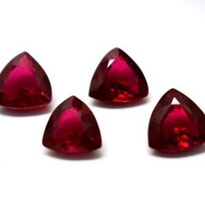 May include: Four triangular red gemstones with a faceted cut.
