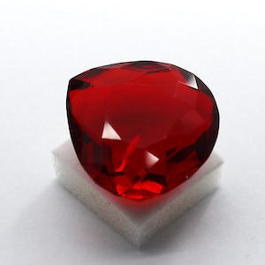 Puede incluir: Un gran corazón de cristal rojo facetado. El corazón está sobre una superficie blanca texturizada.