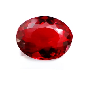 Pode incluir: Uma gema de cor vermelho profundo e vibrante com formato oval e corte facetado. A pedra apresenta numerosas facetas geométricas que refletem a luz, criando uma aparência brilhante e cintilante em toda a sua superfície polida.