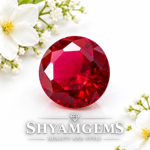 May include: A round, faceted, deep red gemstone with a brilliant cut, positioned centrally. The text SHYAMGEMS QUALITY AND STYLE is printed below the stone, accompanied by a small diamond icon. White flowers are visible in the corners.