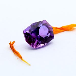 May include: A purple gemstone with a faceted cut. The gemstone is octagonal in shape and has a slight purple to pink gradient.
