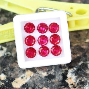 May include: A white tray with nine round, red gemstones. The gemstones are arranged in three rows of three.