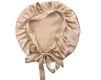 May include: A beige satin bonnet with a gathered edge and a tie closure. The bonnet is designed to protect hair and maintain hairstyles. The satin material has a subtle sheen, and the tie allows for an adjustable fit.
