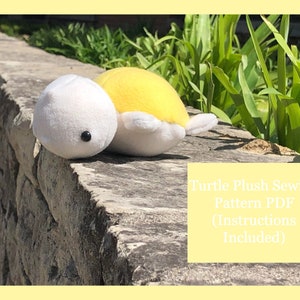 以下が含まれることがあります： 石の壁の上に座っている白と黄色のぬいぐるみのかめのおもちゃ。おもちゃは小さな黒い目があります。テキスト「Turtle Plush Sewing Pattern PDF (Instructions Included)」は黄色の背景にあります。