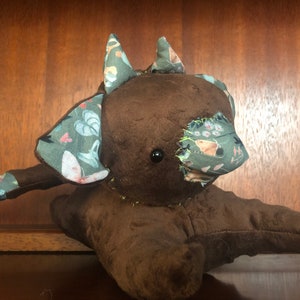 Op de afbeelding: Een bruin pluche speelgoed met een patchwork ontwerp. Het speelgoed heeft een lange staart en twee oren met een bloemenpatroon. Het speelgoed heeft een zwart knoopoog.