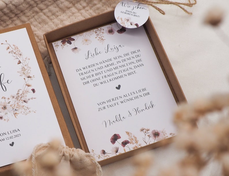 May include: A white card with a floral design and the text "Liebe Luiza. Da werden H&auml;nde sein, die dich tragen und Arme, in denen du sicher bist und Menschen, die dir ohne fragen zeigen, dass du willkommen bist. Von Herzen alles Liebe zur Taufe w&uuml;nschen dir Malita & Hendrik"