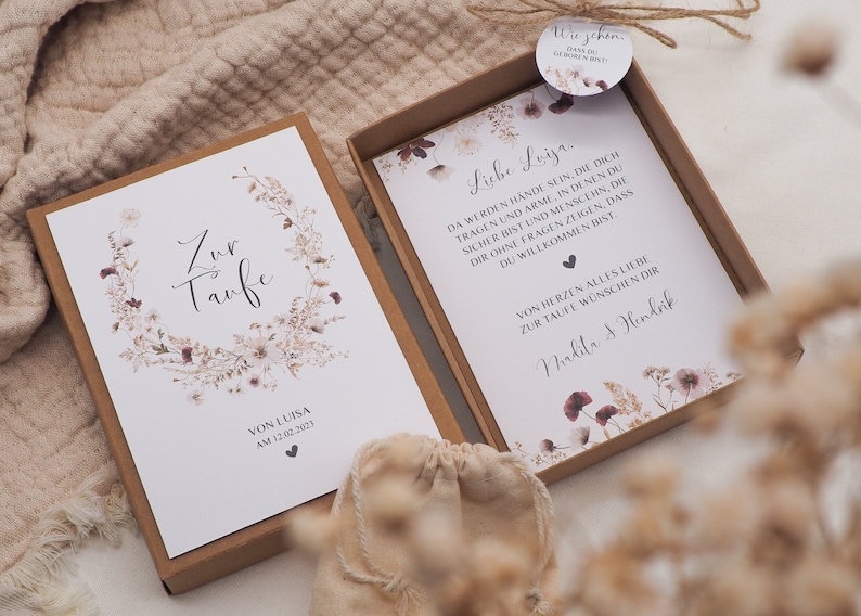 May include: A white card with a floral wreath and the text "Zur Taufe" (German for "For the Baptism") and "Von Luisa am 12.02.2023". A second white card with the text "Liebe Luisa, Da werden H&auml;nde sein, die dich tragen und Arme, in denen du sicher bist und Menschen, die dir ohne Fragen zeigen, dass du willkommen bist. Von Herzen alles Liebe zur Taufe w&uuml;nschen dir Nadja & Hendrik".