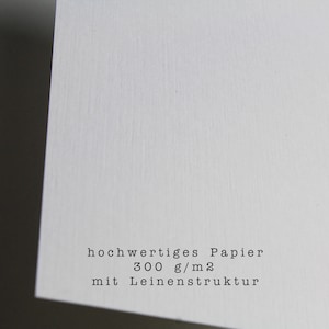 May include: Close-up of a white textured paper with the text "hochwertiges Papier 300 g/m2 mit Leinenstruktur".